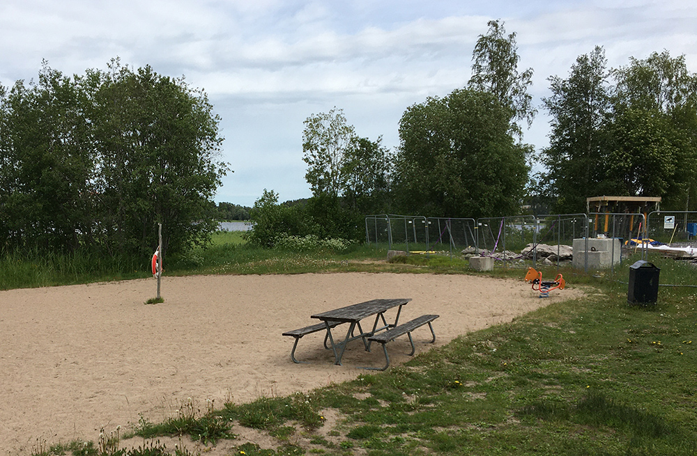 På stranden finns en bord med bänkar bredvid en lekgunga.