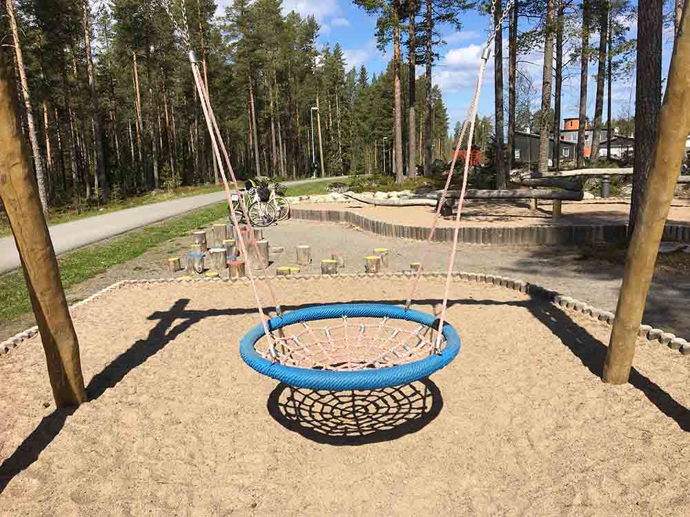 En stor kompisgunga i blått hänger ovanför en sandfylld lekplats