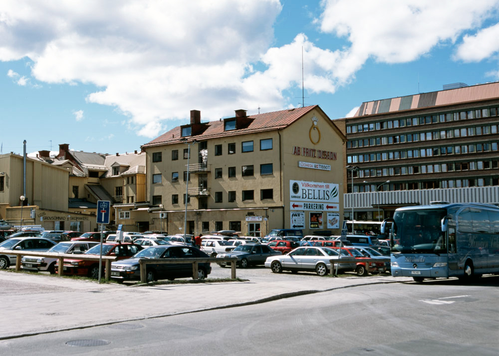 Vy över kvarter med bilparkering och större hus i bakgrunden.