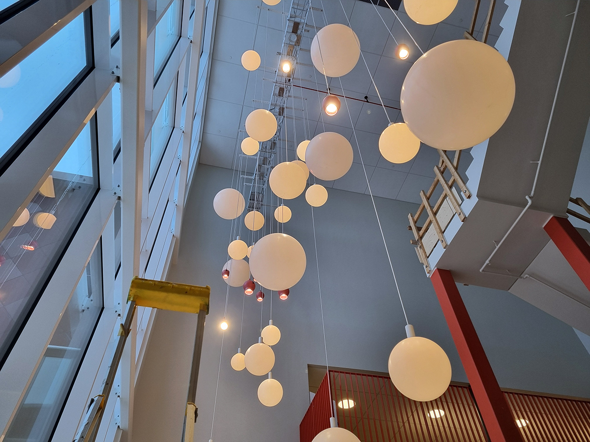 Bild på globformade lampor som hänger från taket som är flera våningar upp. En trapp går uppåt med räcken som fortfarande är av tillfällig träkonstruktion