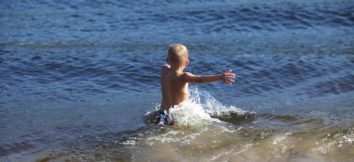Ett barn som badar vid ett friluftsbad och plaskar i vattnet
