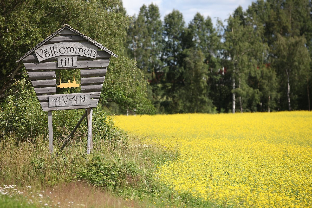 Välkomstskylt för Avan med gula vält och gröna skogar